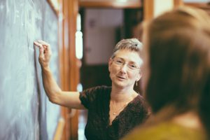 Teacher at chalkboard explaining math formulas to young female teenage student. Personal Perspective, Selective focus, small DOF. Natural interior light.